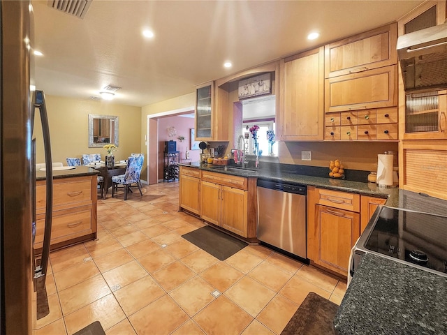 kitchen featuring a sink, visible vents, wall chimney range hood, appliances with stainless steel finishes, and glass insert cabinets