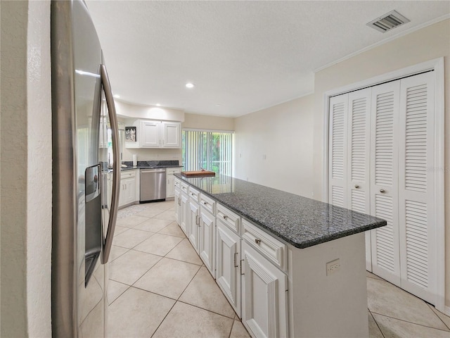 kitchen featuring dark stone counters, stainless steel appliances, light tile patterned floors, a kitchen island, and white cabinetry