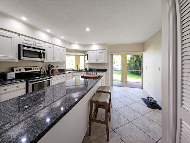 kitchen featuring plenty of natural light, appliances with stainless steel finishes, dark stone counters, and white cabinets