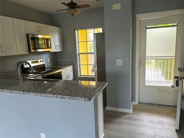 kitchen with stone counters, appliances with stainless steel finishes, white cabinetry, kitchen peninsula, and light hardwood / wood-style flooring