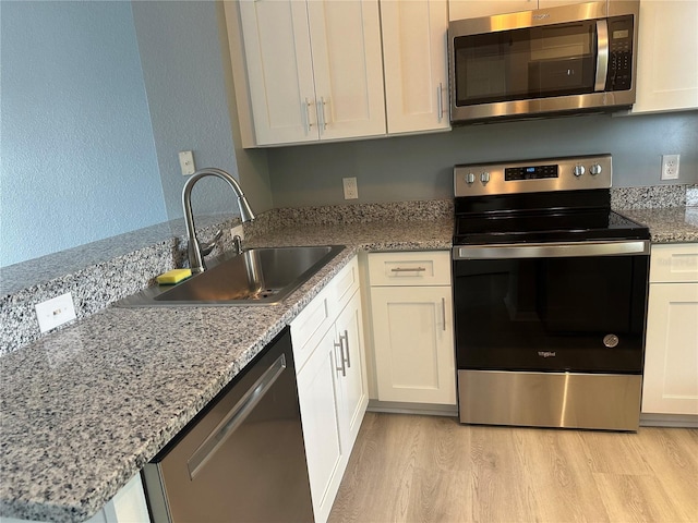 kitchen with sink, light hardwood / wood-style flooring, appliances with stainless steel finishes, white cabinetry, and light stone countertops