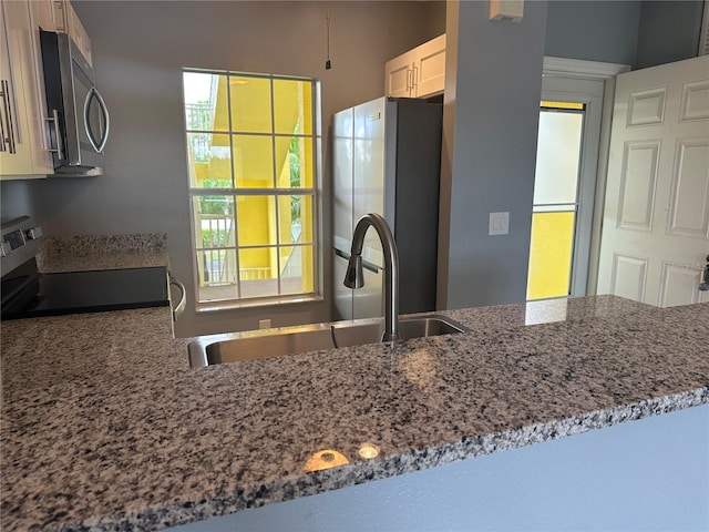 kitchen featuring sink, kitchen peninsula, stainless steel appliances, light stone countertops, and white cabinets