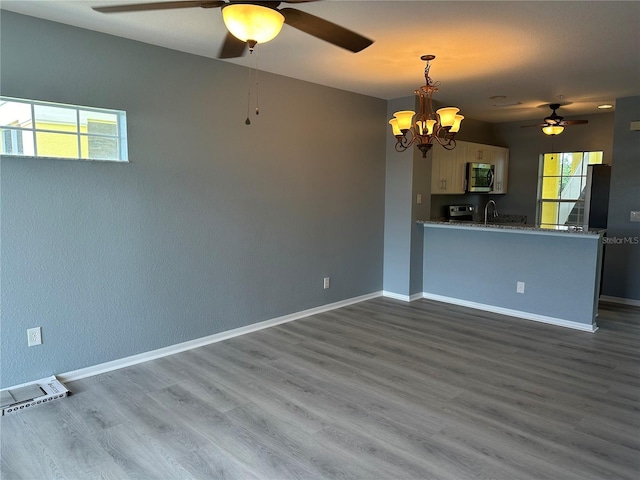 interior space featuring sink, decorative light fixtures, dark hardwood / wood-style flooring, kitchen peninsula, and ceiling fan with notable chandelier