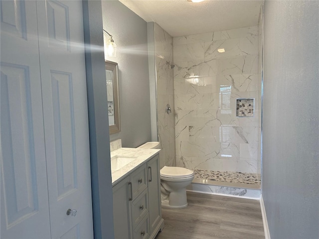 bathroom featuring hardwood / wood-style floors, vanity, a tile shower, a textured ceiling, and toilet