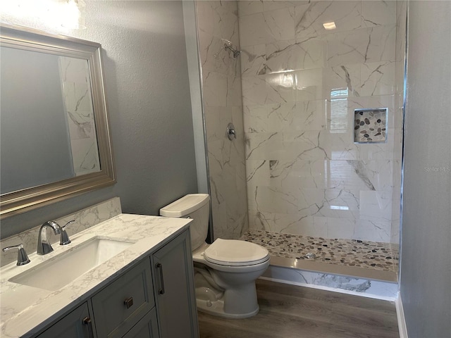 bathroom featuring hardwood / wood-style floors, vanity, a tile shower, and toilet