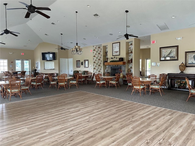 interior space with a stone fireplace, ceiling fan with notable chandelier, high vaulted ceiling, and light hardwood / wood-style floors