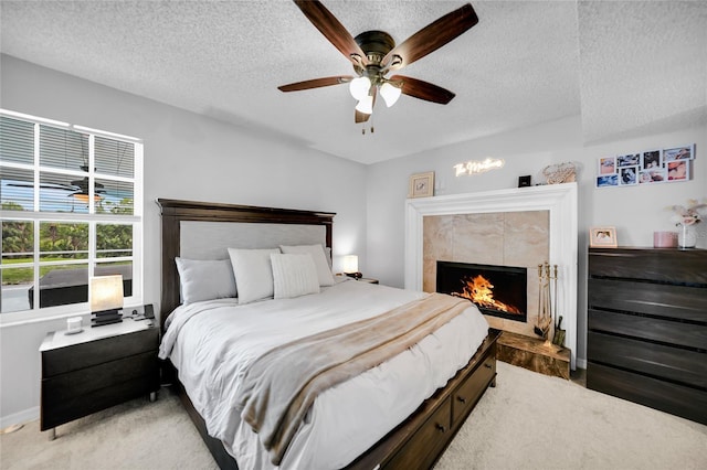 carpeted bedroom featuring ceiling fan, a tiled fireplace, and a textured ceiling