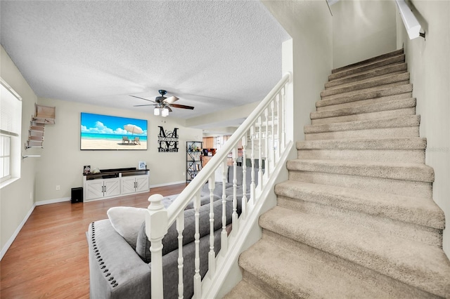 stairs featuring ceiling fan, wood-type flooring, and a textured ceiling