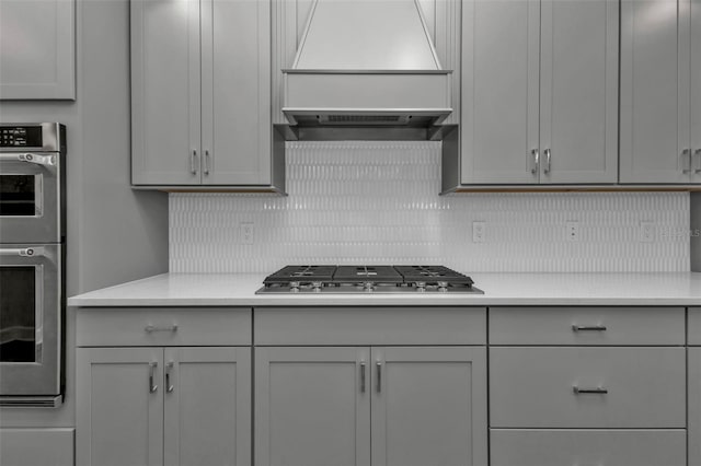 kitchen with backsplash, custom range hood, appliances with stainless steel finishes, and gray cabinets