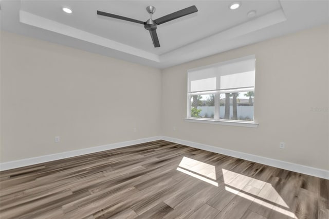 empty room featuring hardwood / wood-style flooring, a tray ceiling, and ceiling fan