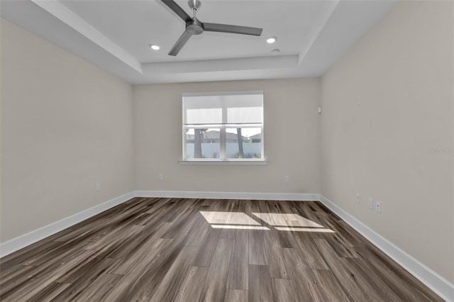 unfurnished room featuring ceiling fan, dark wood-type flooring, and a tray ceiling