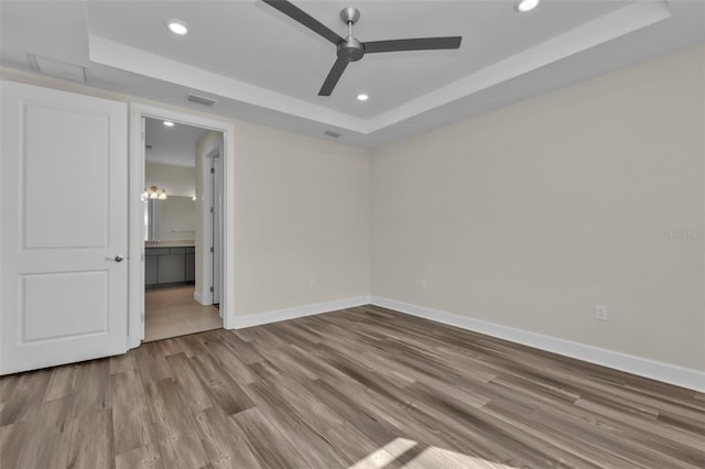 unfurnished bedroom with connected bathroom, ceiling fan, a raised ceiling, and hardwood / wood-style flooring