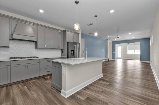 kitchen featuring high quality fridge, custom exhaust hood, gas cooktop, a center island with sink, and gray cabinets