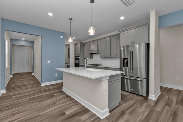 kitchen with gray cabinets, custom range hood, high end fridge, and an island with sink