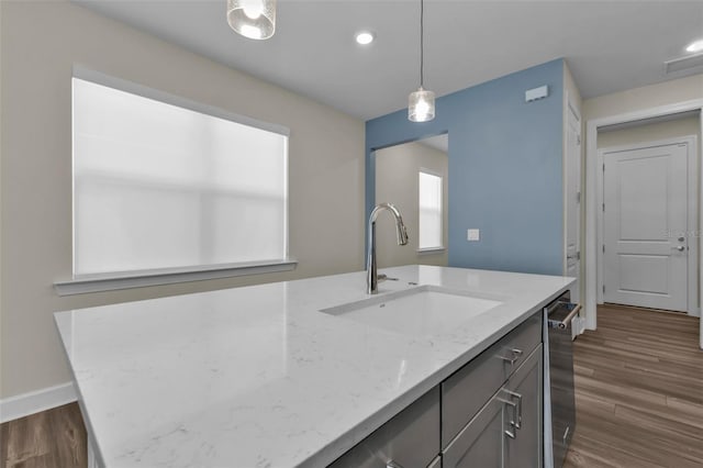 kitchen featuring stainless steel dishwasher, decorative light fixtures, sink, light stone countertops, and an island with sink