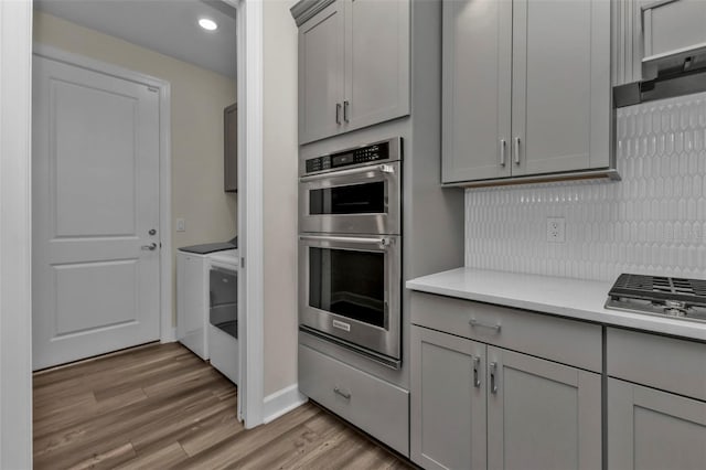 kitchen featuring light stone countertops, appliances with stainless steel finishes, light hardwood / wood-style floors, decorative backsplash, and gray cabinetry