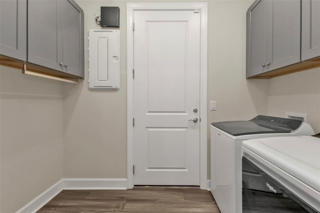 laundry area featuring washer and clothes dryer, electric panel, light hardwood / wood-style floors, and cabinets