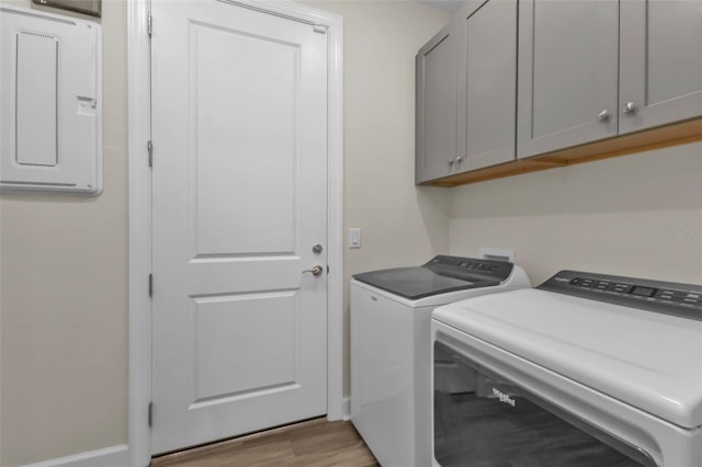 clothes washing area with separate washer and dryer, electric panel, light hardwood / wood-style floors, and cabinets