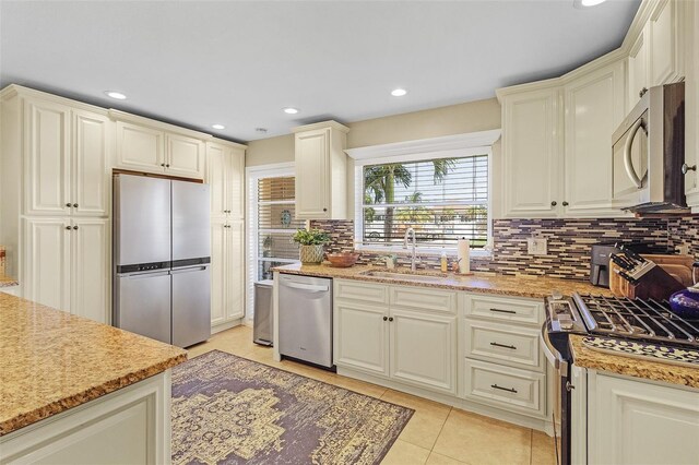 kitchen featuring light tile patterned floors, backsplash, cream cabinetry, stainless steel appliances, and sink