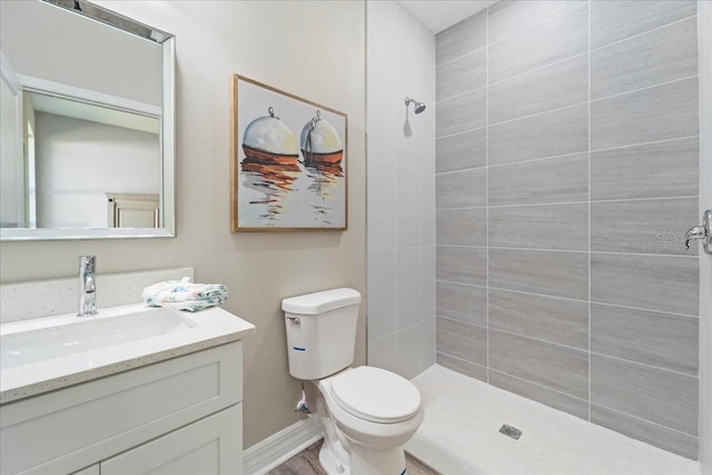 bathroom with baseboards, tiled shower, vanity, and toilet