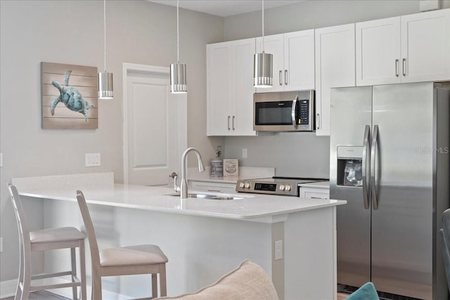 kitchen featuring stainless steel appliances, a sink, white cabinetry, a kitchen breakfast bar, and decorative light fixtures