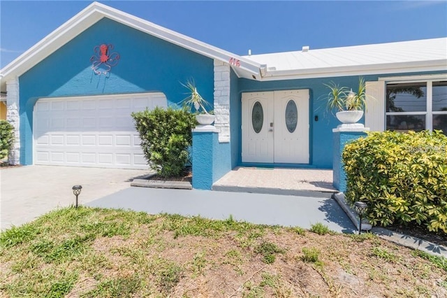 property entrance with stucco siding, an attached garage, and driveway