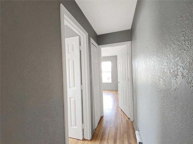 hallway with light wood-style floors and a textured wall