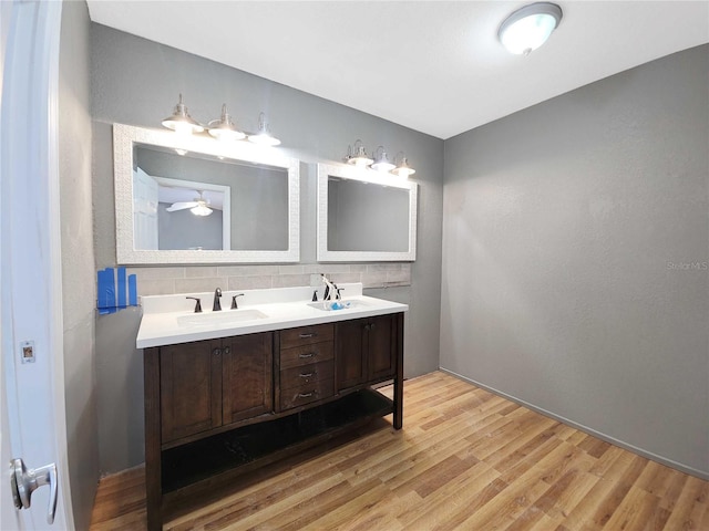 bathroom featuring a sink, decorative backsplash, wood finished floors, and double vanity