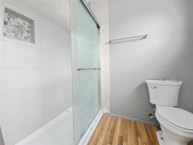 bathroom featuring a shower stall, toilet, wood finished floors, and a textured wall