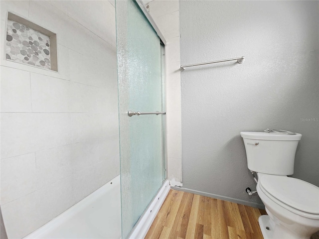 bathroom with toilet, wood finished floors, a stall shower, and a textured wall