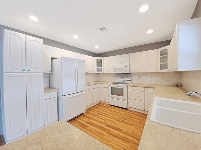 kitchen featuring visible vents, a sink, tasteful backsplash, white appliances, and light wood finished floors