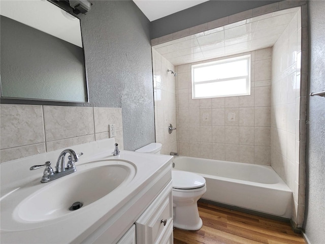 bathroom featuring toilet, shower / washtub combination, wood finished floors, vanity, and a textured wall