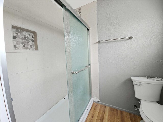 bathroom with a shower stall, toilet, a textured wall, and wood finished floors