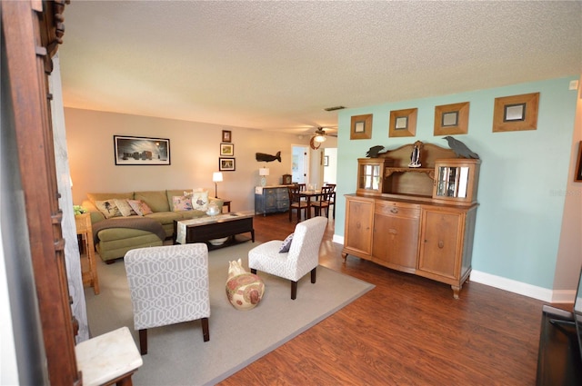 living room with a textured ceiling, ceiling fan, and dark wood-type flooring