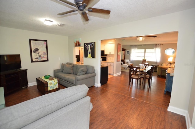 living room featuring ceiling fan, dark wood-type flooring, and a textured ceiling