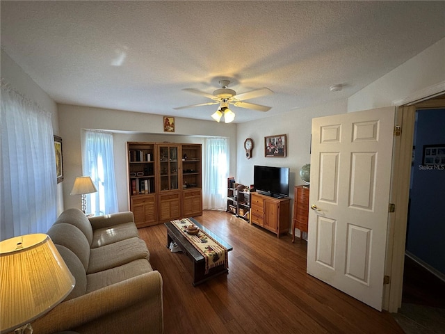 living room with a textured ceiling, dark hardwood / wood-style flooring, and ceiling fan