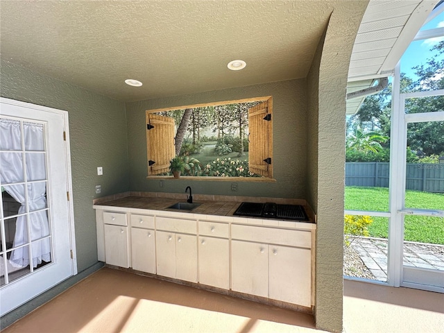 bar with sink, a textured ceiling, white cabinets, and a healthy amount of sunlight