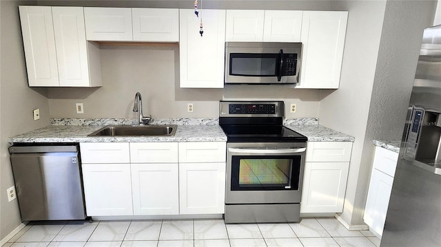 kitchen with stainless steel appliances, white cabinetry, sink, and light stone countertops