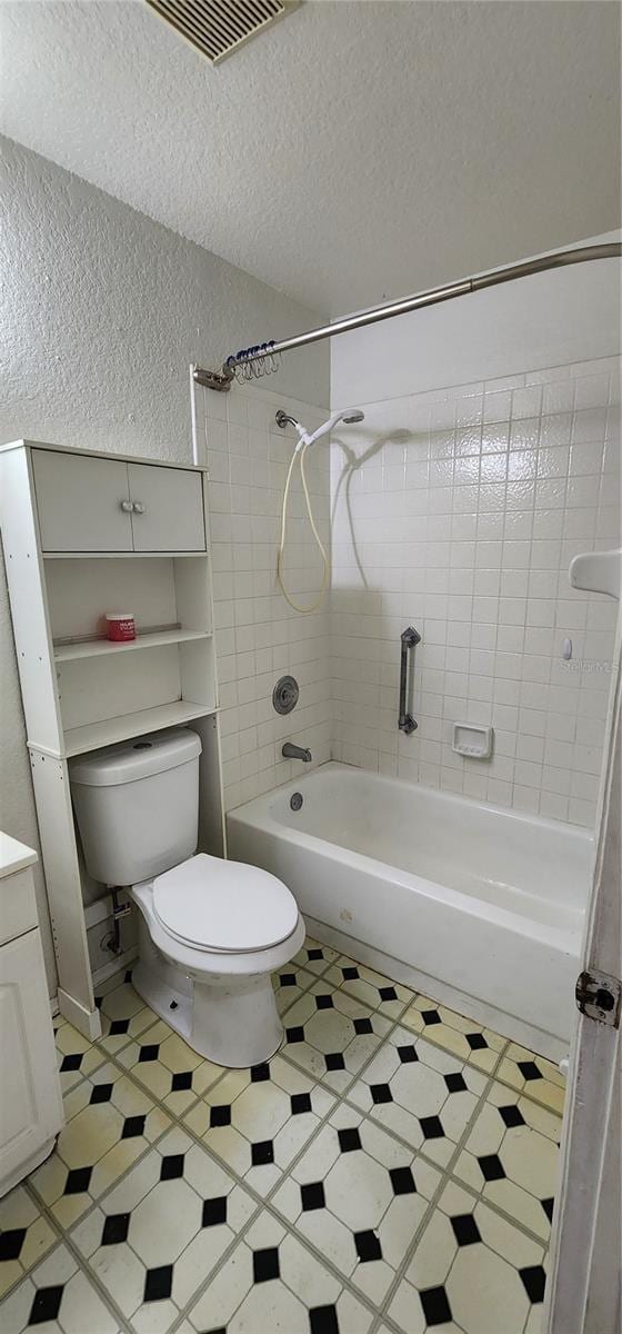 full bathroom with toilet, vanity, a textured ceiling, and tiled shower / bath