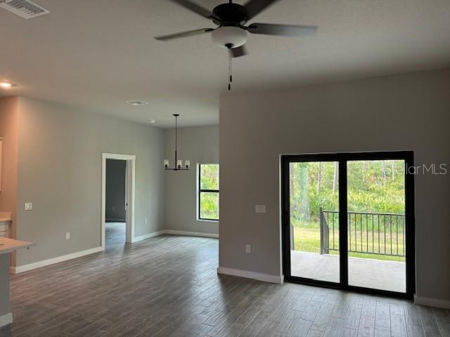 empty room with ceiling fan with notable chandelier, plenty of natural light, and dark hardwood / wood-style floors