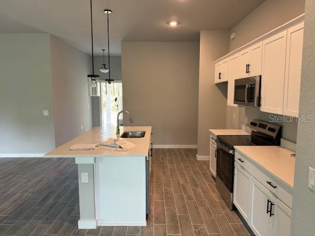 kitchen featuring white cabinets, stainless steel appliances, an island with sink, sink, and hanging light fixtures