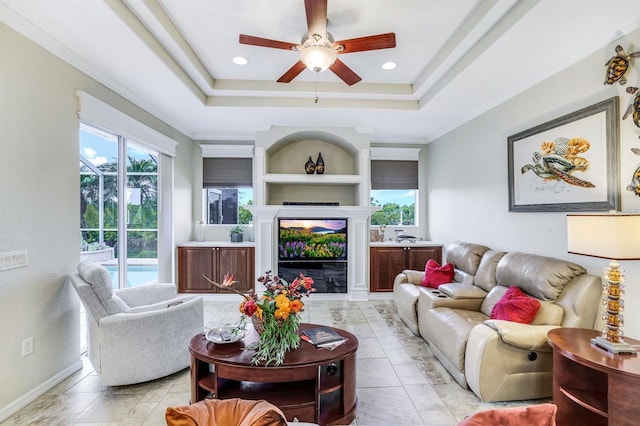 living room featuring ceiling fan, ornamental molding, and a tray ceiling