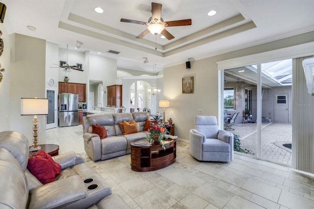 living room featuring a raised ceiling, ornamental molding, and ceiling fan with notable chandelier