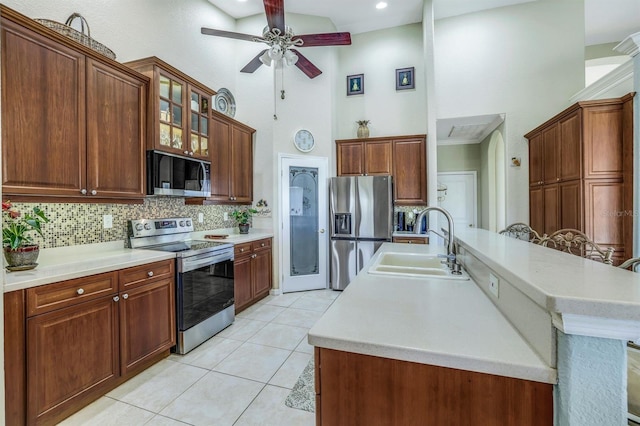 kitchen featuring sink, a towering ceiling, stainless steel appliances, a kitchen island with sink, and decorative backsplash