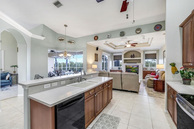 kitchen with ceiling fan with notable chandelier, dishwasher, sink, a raised ceiling, and a center island with sink