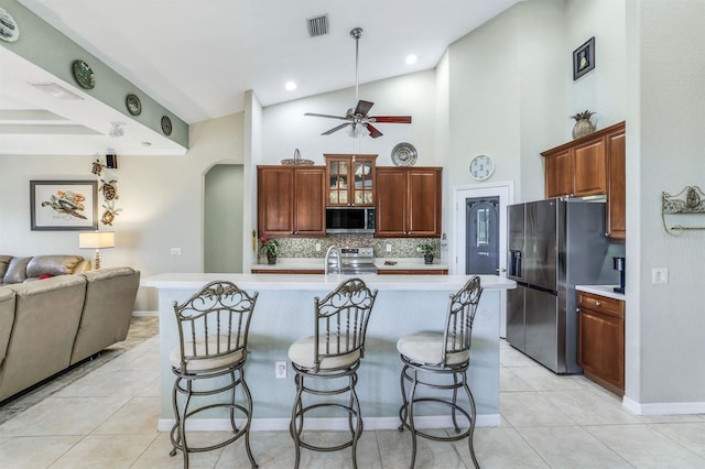 kitchen featuring high vaulted ceiling, a breakfast bar area, backsplash, a kitchen island with sink, and stainless steel appliances