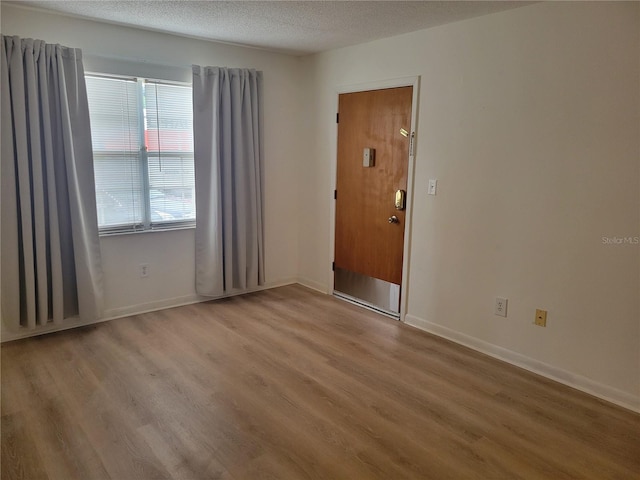 empty room with a textured ceiling, wood finished floors, and baseboards