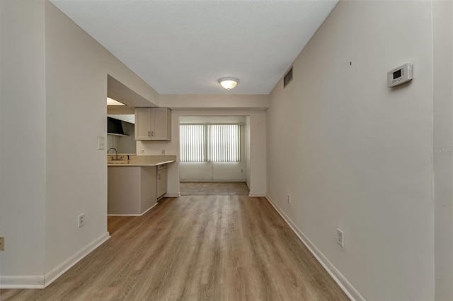 unfurnished living room with light wood-style floors, baseboards, visible vents, and a sink