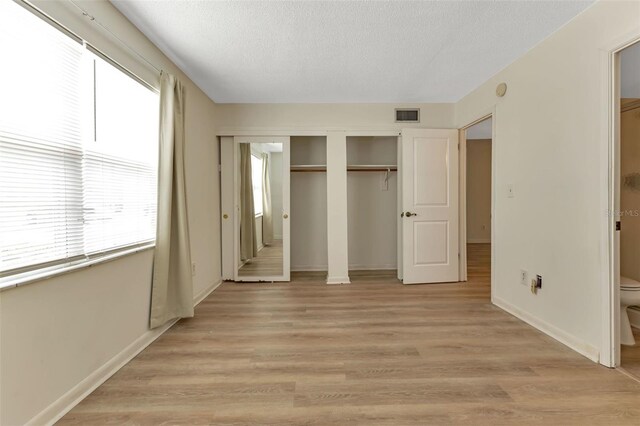 unfurnished bedroom with a textured ceiling, visible vents, baseboards, light wood-style floors, and a closet