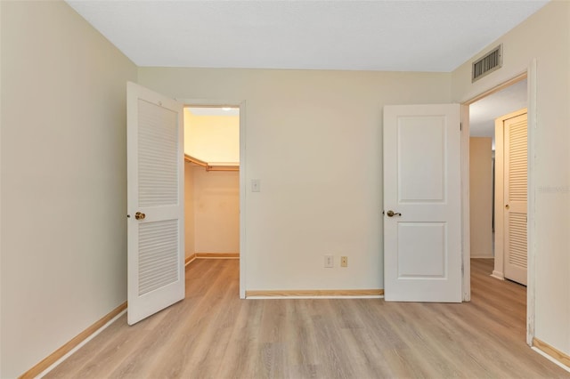 unfurnished bedroom featuring light wood-style floors, a walk in closet, visible vents, and baseboards